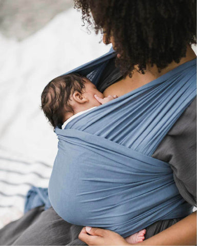 Baby held by mom in a Solly Wrap nurses with eyes closed