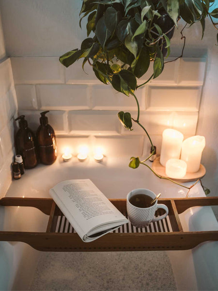 Open book and tea on a tray above a candle-lit bubble bath