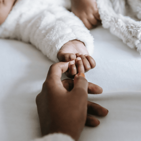 Mother with dark skin tone hold hand of sleeping baby