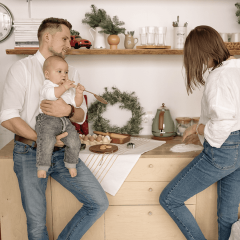 Father holds baby in kitchen while mother makes Christmas cookies