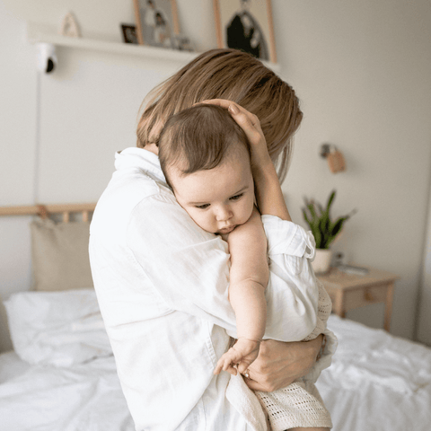 Mother with light skin tone holds sleeping baby in nursery