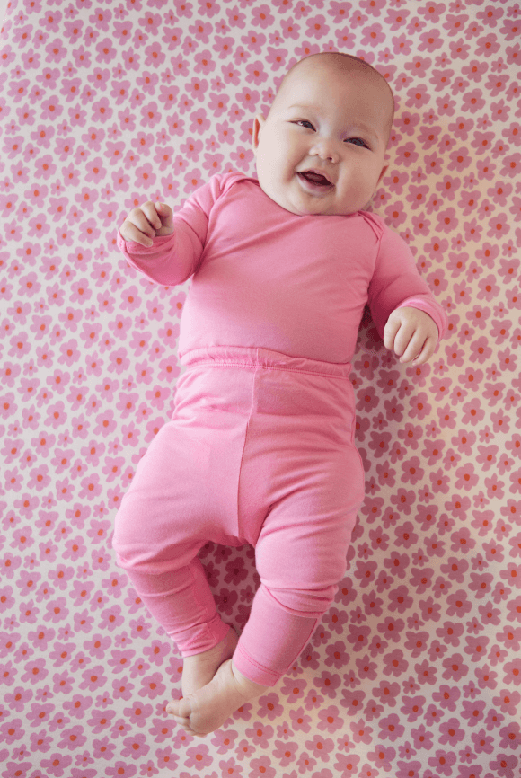 Smiling baby wearing an Iconic Pink sleeper, laying on a Ditsy Floral crib sheet