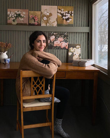 Woman sits on chair with arms crossed over the back and smiles in artist studio