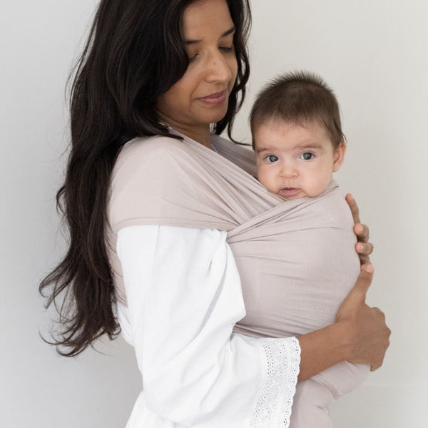 Woman with long black hair looks at baby wrapped in the Petal Solly Wrap