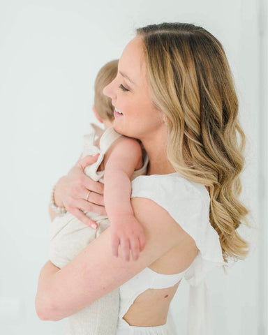 Woman holds baby close in white dress