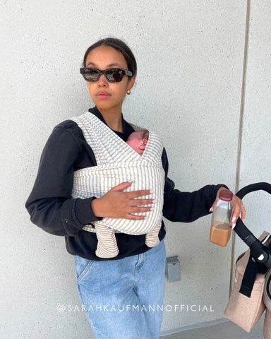 Stylish mom has one hand on stroller and one hand on her baby in the Natural Gray Stripe Solly Wrap