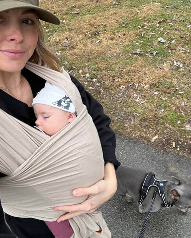 Woman takes selfie while walking dog while wearing baby in Spelt Solly Wrap