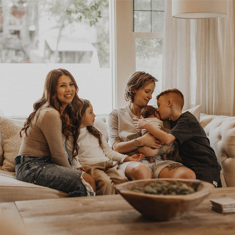 Family (2 moms, 2 sons, and 1 daughter) sit on couch.