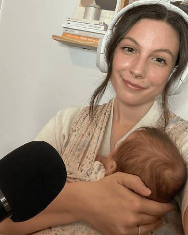 Woman wearing headphones smiles holding baby with a microphone in front of her