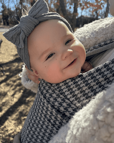 Baby with large gray bow smiles in Stormy Houndstooth Solly Wrap