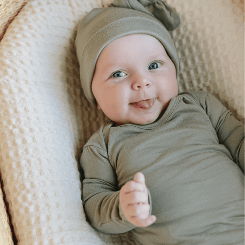 Baby with light skin tone and blue eyes smiles in Mist Solly Sleeper and Knotted Hat