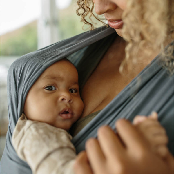 Woman with curly hair looks down at baby in Swell Solly wrap