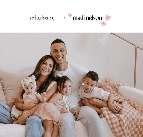 Mother and father on couch with 3 young children in their arms smiling.