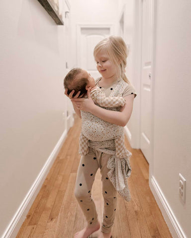 Little girl holds baby sibling in Myrtle Solly Wrap