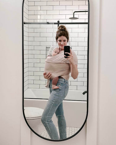 Woman takes mirror selfie in bathroom wearing baby in Heritage Blush Wrap