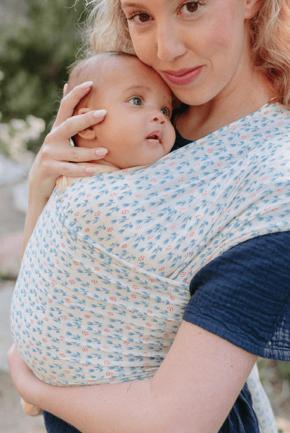 Blonde mother holds baby in a floral Solly wrap and smiles