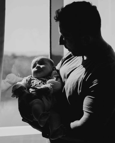Black and white image of man standing in front of a window holding baby