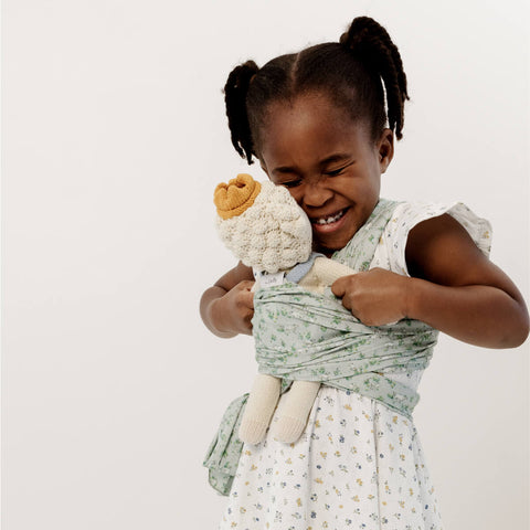 Young girl with dark skin tone smiles while wearing stuffed animal in the Solly Dolly Wrap