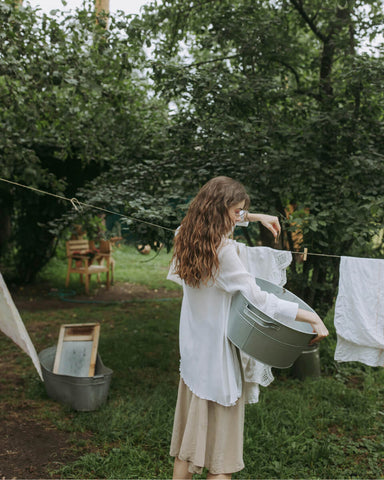 Woman with brown, wavy hair hangs linens on outdoor clothesline