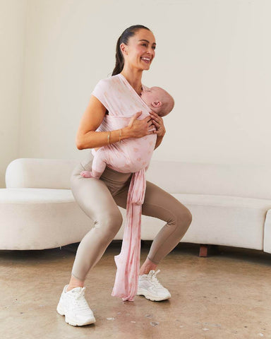 Woman wearing active wear squats while wearing baby with Bloom Solly Wrap