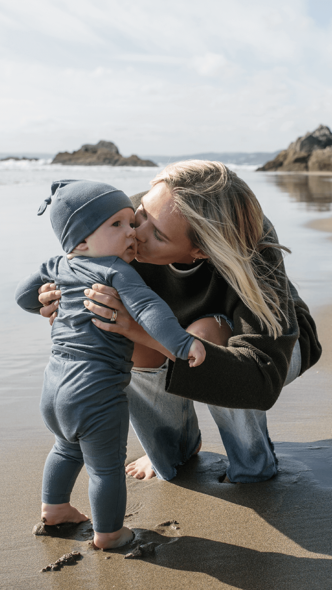 Mother kissing baby barefoot on the beach