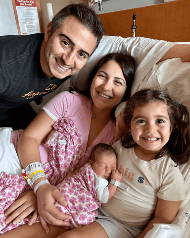 Mother, father, and young daughter smile holding new baby in the hospital