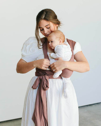 Mother holds baby's leg and lifts it into the cross section of the Cottage Rose Solly Wrap