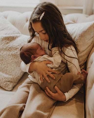 Young girl with long hair, holds baby in her lap and looks lovingly at him