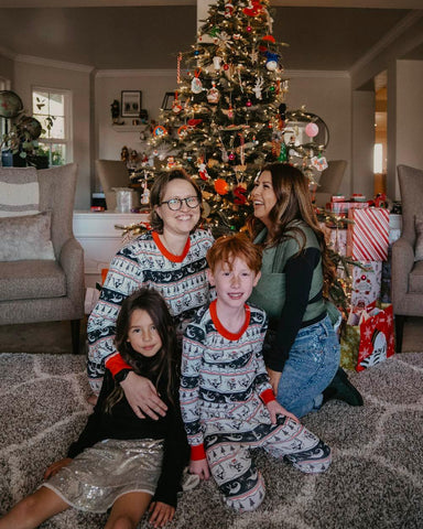Happy family with two moms, and three children smile in front of a Christmas tree