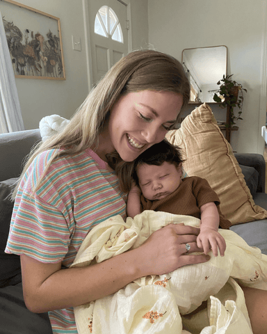 Woman with long blond hair smiles and embraces baby sitting on her lap