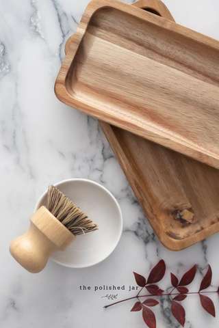 Dos bandejas de madera y un cepillo para jabón en un mostrador de baño de mármol