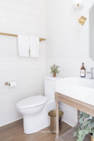 Espacio de baño blanco moderno decorado con accesorios dorados y dispensadores de jabón con botellas de vidrio