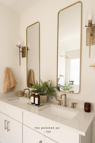 Espacio de baño blanco moderno decorado con accesorios dorados y dispensadores de jabón con botellas de vidrio