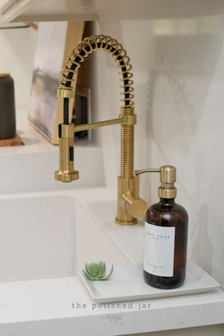 The Polished Jar Glass Bottle Soap Dispenser Next to Gold Faucet