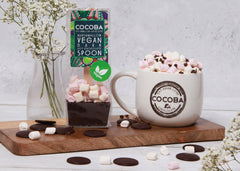Vegan dark hot chocolate spoon next to a cup of hot chocolate topped with vegan whipped cream and marshmallows