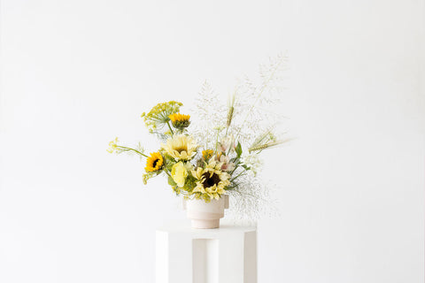 Our Prairie arrangement, inspired by the beauty of grassy prairie land, is a show-stopping floral design. Combining sunflowers, grasses, alstroemeria, and larkspur, this classic combination of perennials is full of texture. Perfect for making a statement in any space. Designed in a white ceramic vase.