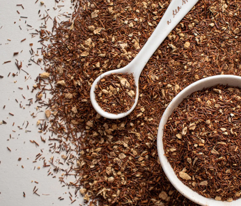 Image of loose leaf tea spilled on a surface with a white ceramic bowl and spoon.