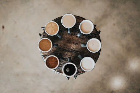 Coffees with varying levels of milk arranged in a circle on a wooden table.