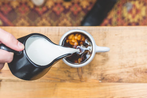 Cream pouring into cup of coffee