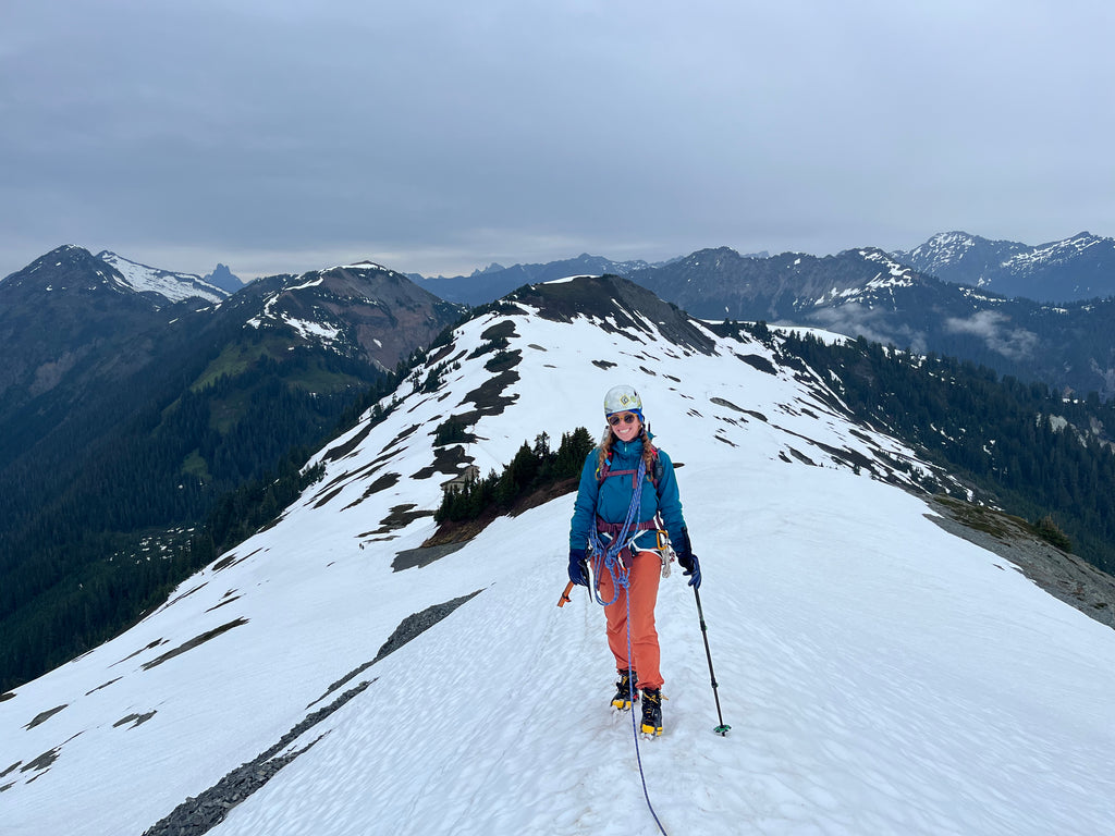 Woman smiles on snowy ridge while wearing La Sportiva Aequilibrium LT GTX Mountain Boots with crampons