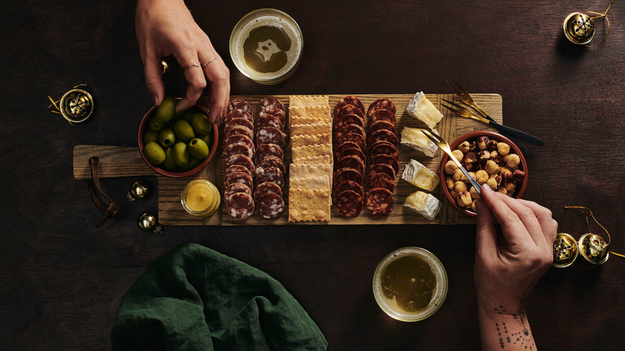 Hands enjoying a happy hour charcuterie kit on a board, with wine