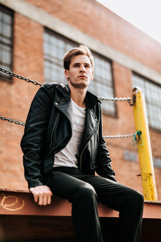 Model wearing a black leather jacket with a white shirt underneath along with dark jeans. 