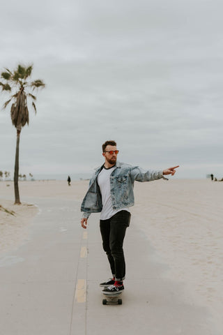 Model wearing a denim jacket with a white shirt underneath riding a skateboard.