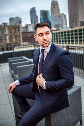 Man on a rooftop over looking a city skyline wearing a navy suit with a pink button down shirt