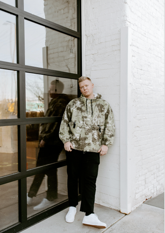 Man wearing camo pullover hoodie, black pants and white tennis shoes