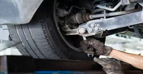 A man's hand is removing the end of the control arm attached to the tire.