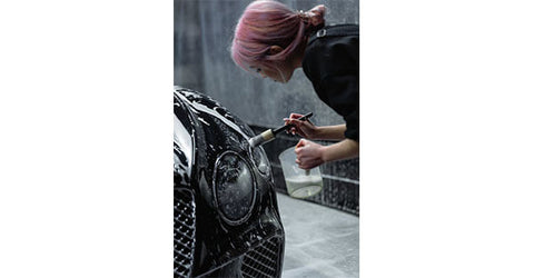 A woman is washing headlights with a fine-bristle brush with soapy water