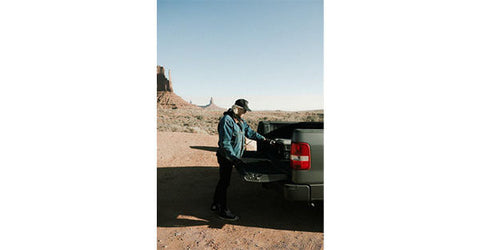 A man in a blue shirt and hat stands in front of a pickup truck