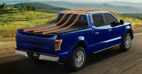 A blue pickup truck with a tonneau cover drives on the road in the mountains.