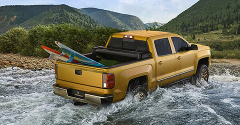 A yellow pickup truck with a full trunk makes waves in the creek.